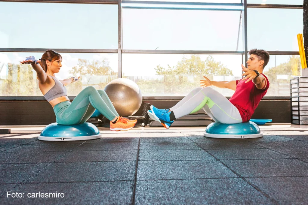 Mann und Frau machen verschiedene Übungen mit dem Balancekissen Bosu im Fitnessstudio - PDPS4R4 - Foto carlesmiro